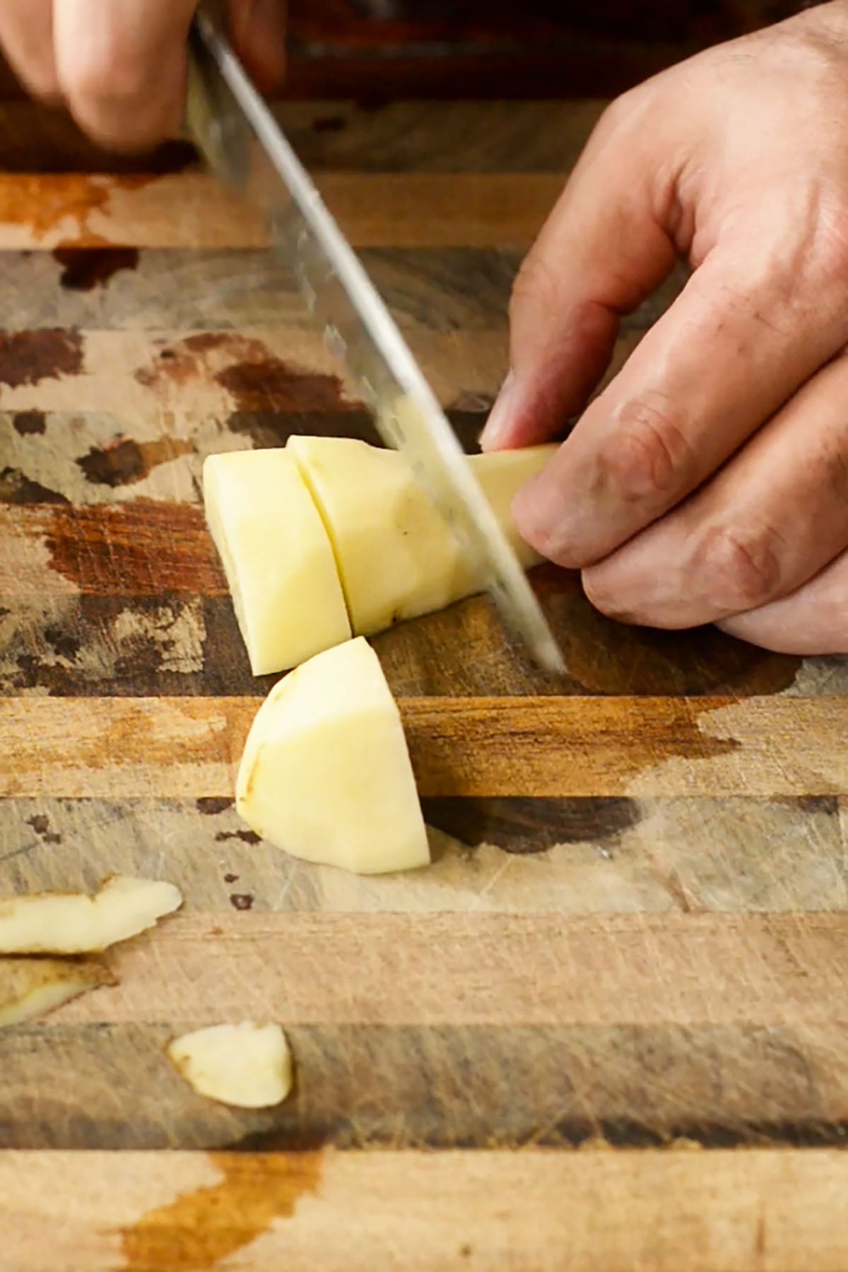 A peeled russet potato be cubed on a wood cutting board.