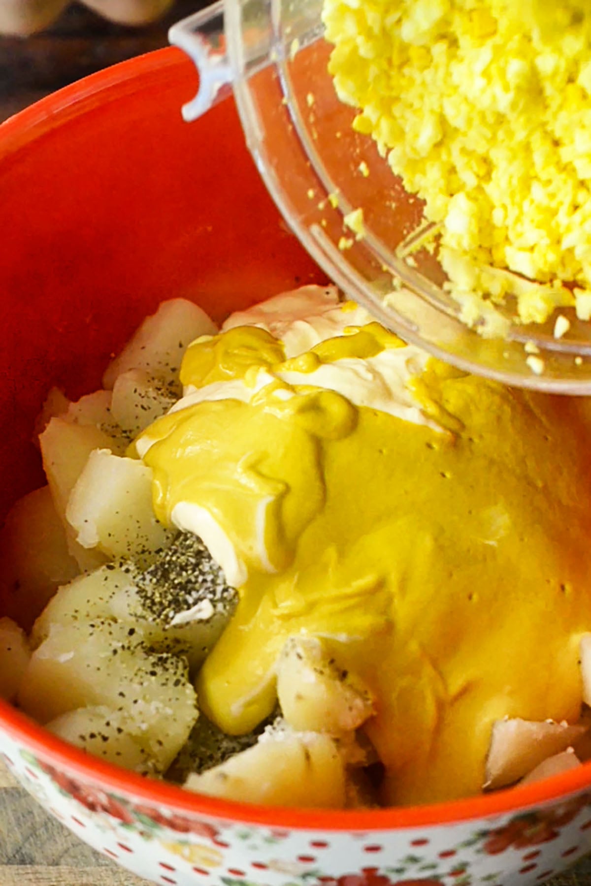Classic Southern potato salad ingredients being poured into a large mixing bowl.