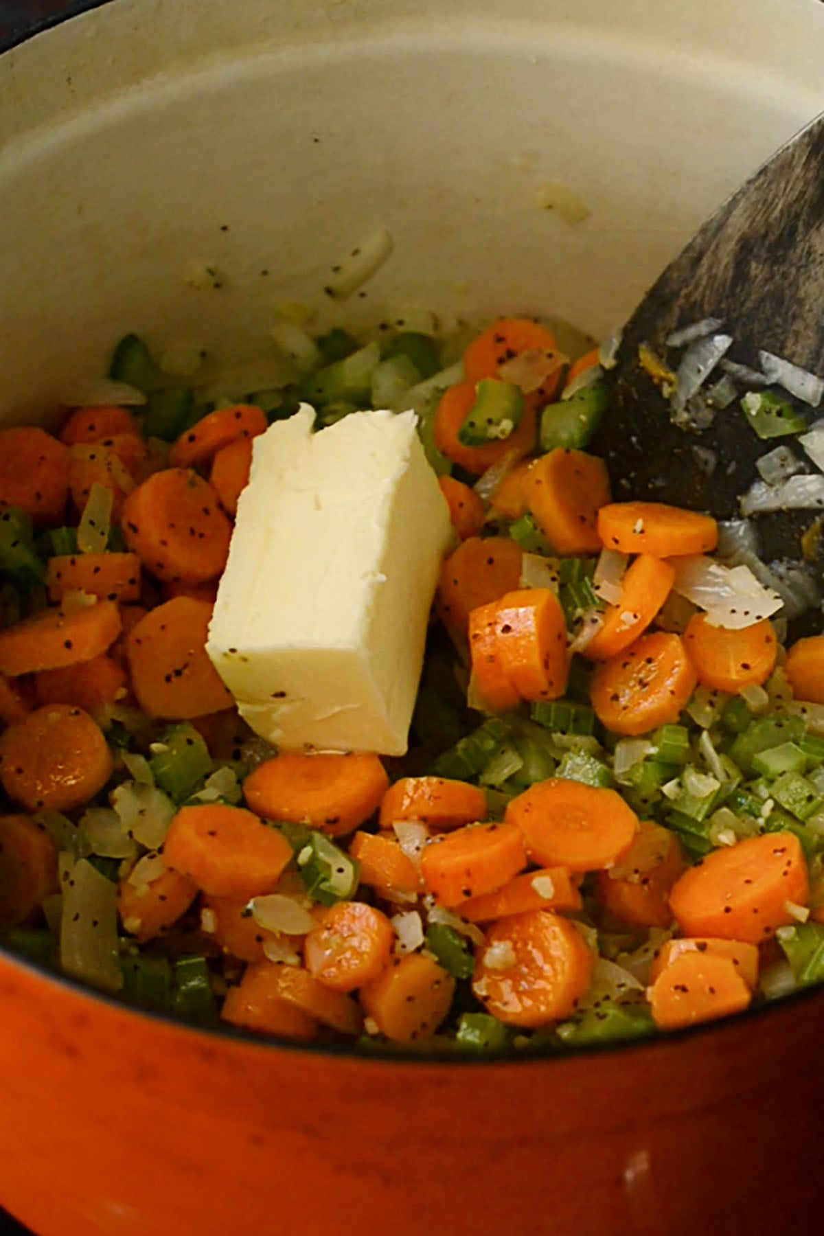 Seasoned sautéed vegetables with butter in a dutch oven with a wooden spatula.