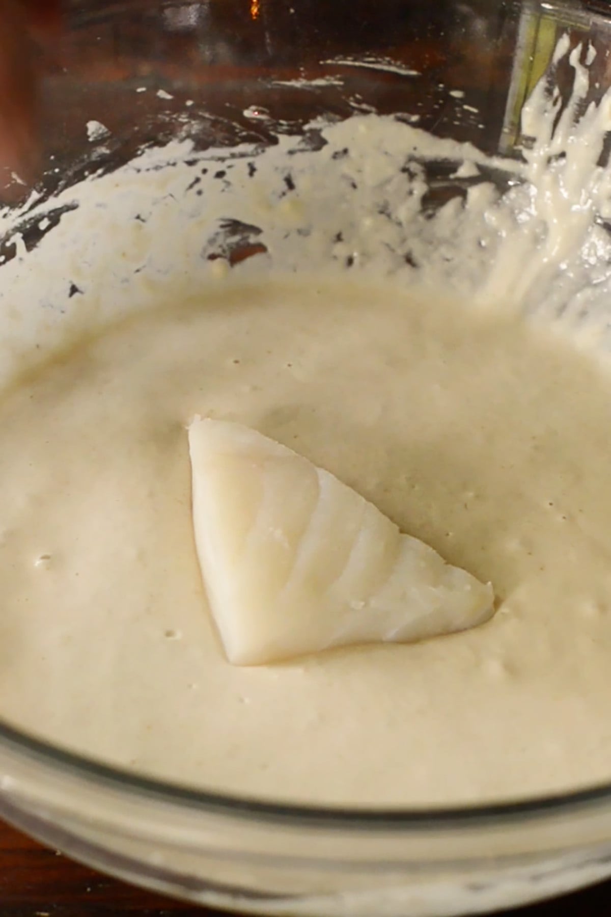 A piece of cod, sliced in a triangle shape in a bowl of batter.