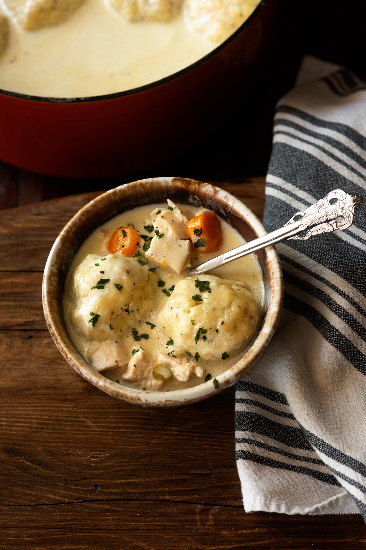 Southern Chicken and Dumplings soup served in a rustic bowl with a vintage soup and garnished with freshly chopped basil.