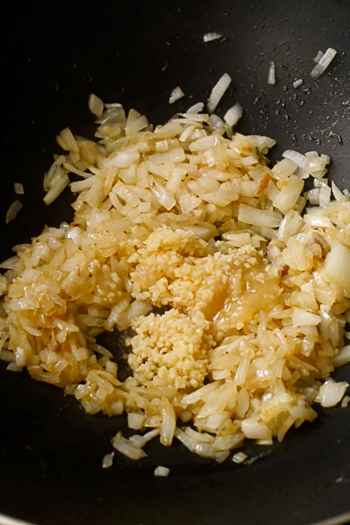 Diced onions, minced garlic, and minced ginger sautéing in a wok.