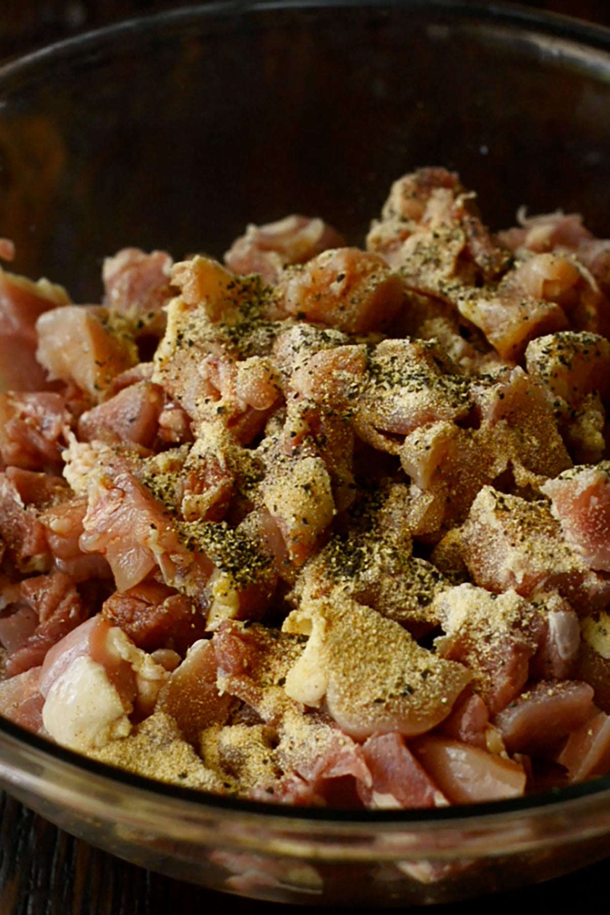 Seasoned cubed chicken thighs in a glass mixing bowl.