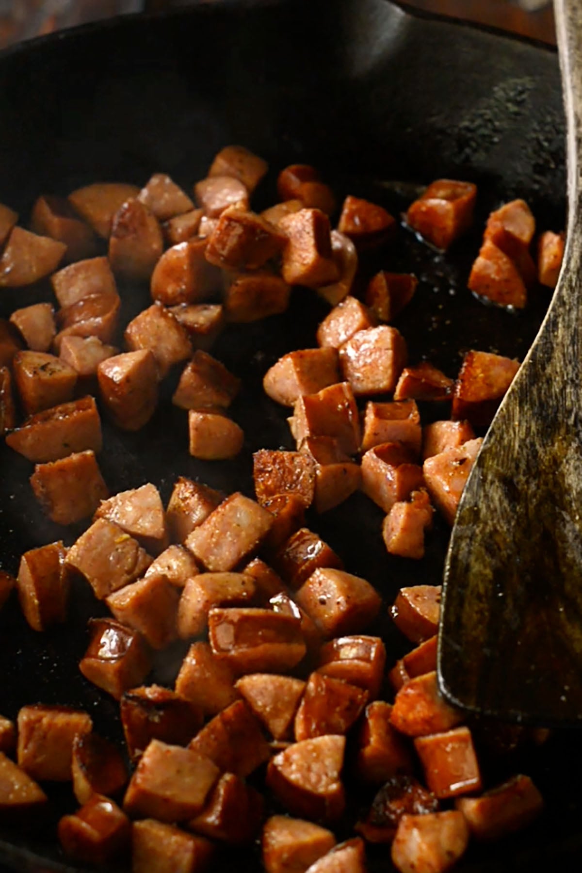 Diced andouille sausage cooking in a cast iron skillet.
