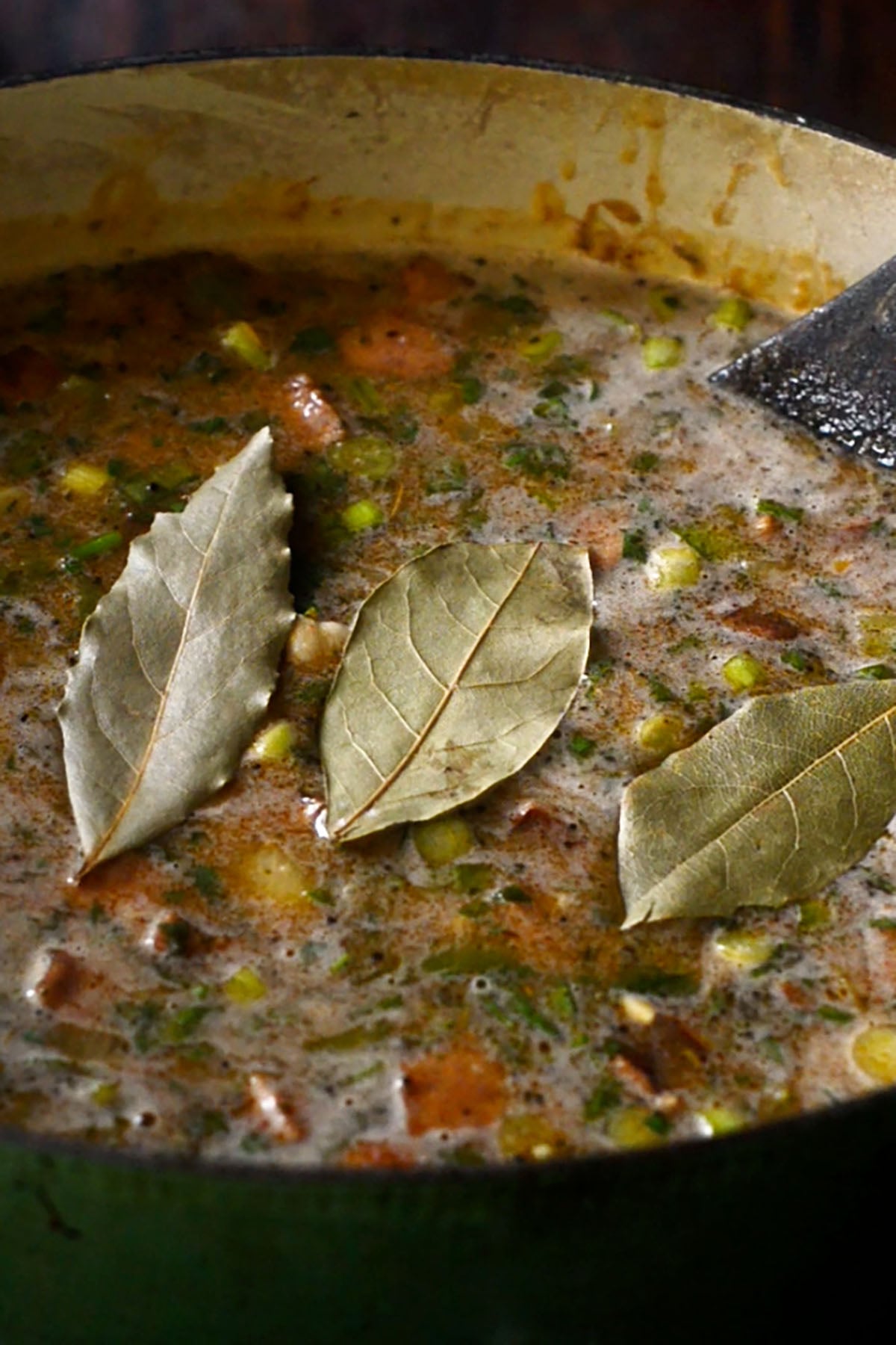 Bay leaves added to a pot of simmering gumbo in a dutch oven.