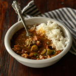 Chicken and sausage gumbo served in a white bowl with a vintage spoon.