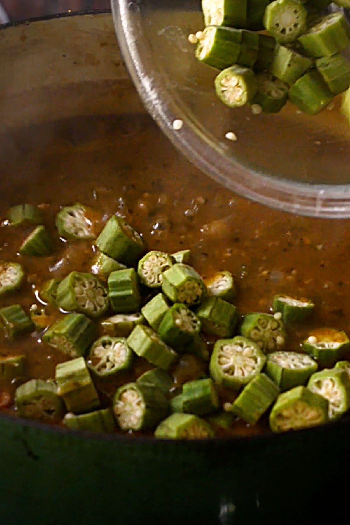 Fresh sliced okra being added to a pot of simmering chicken and sausage gumbo.