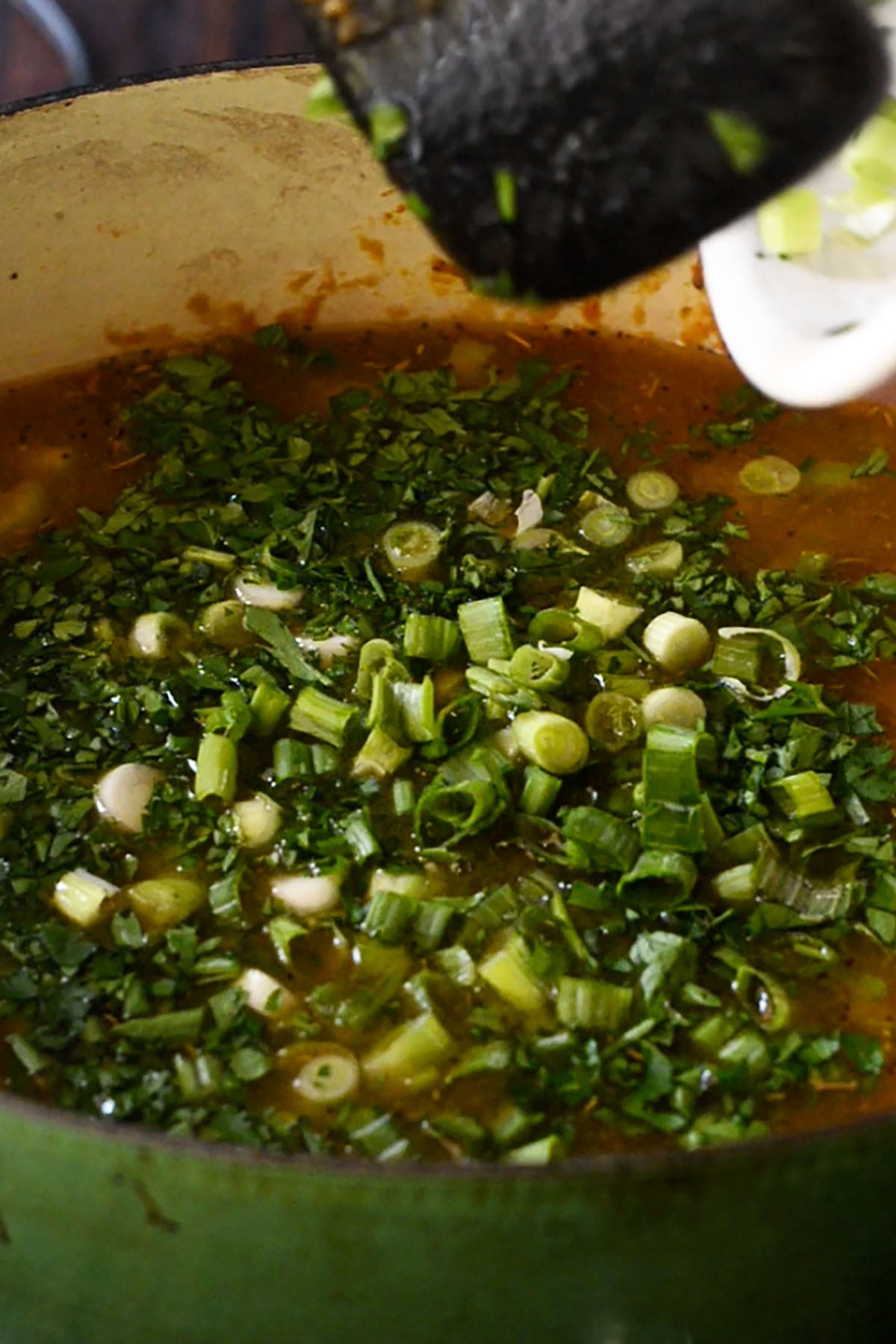 Fresh chopped parsley and sliced green onions being stirred into chicken and sausage gumbo.