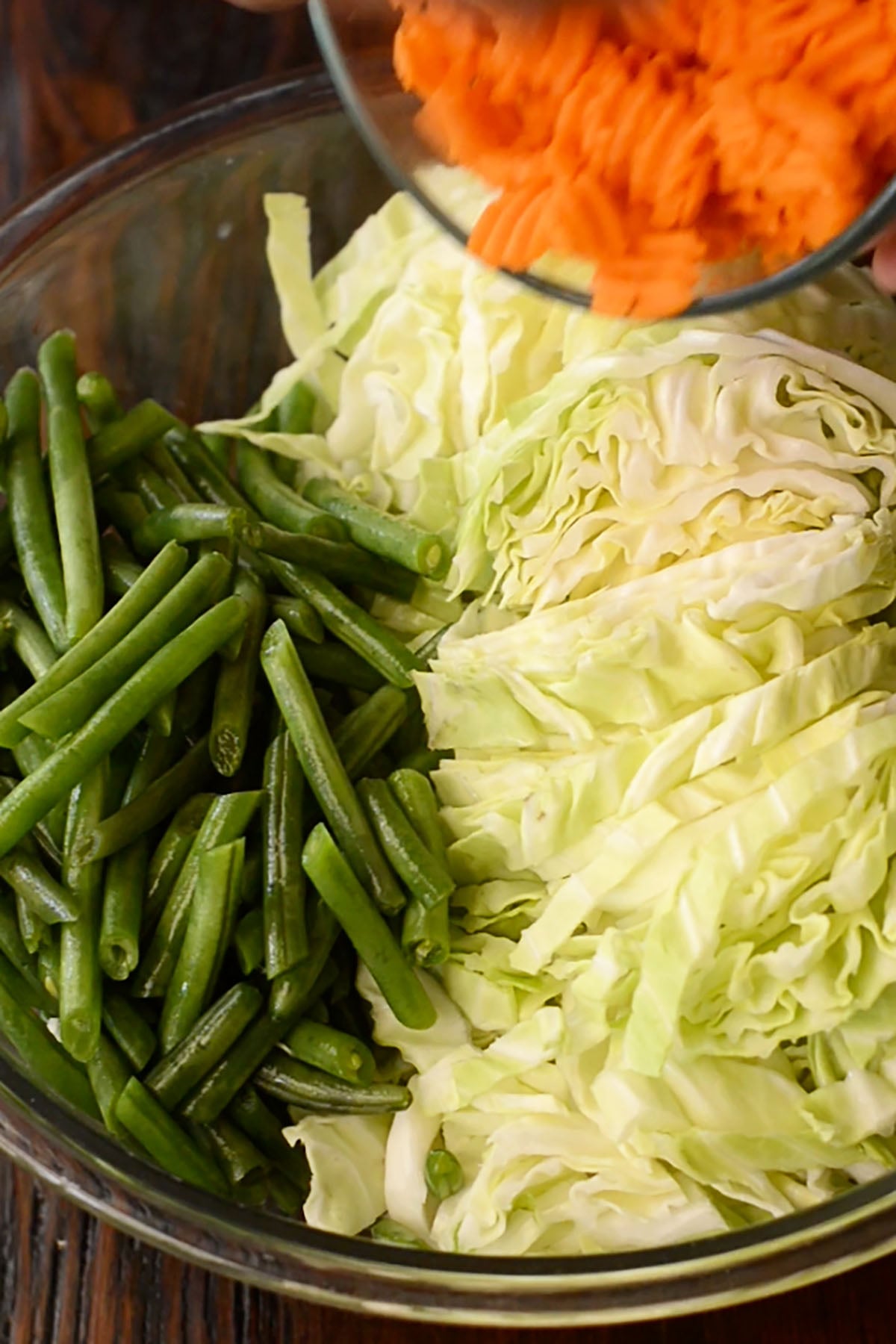 Cabbage, carrots, and green beans sliced and prepared in a mixing bowl.