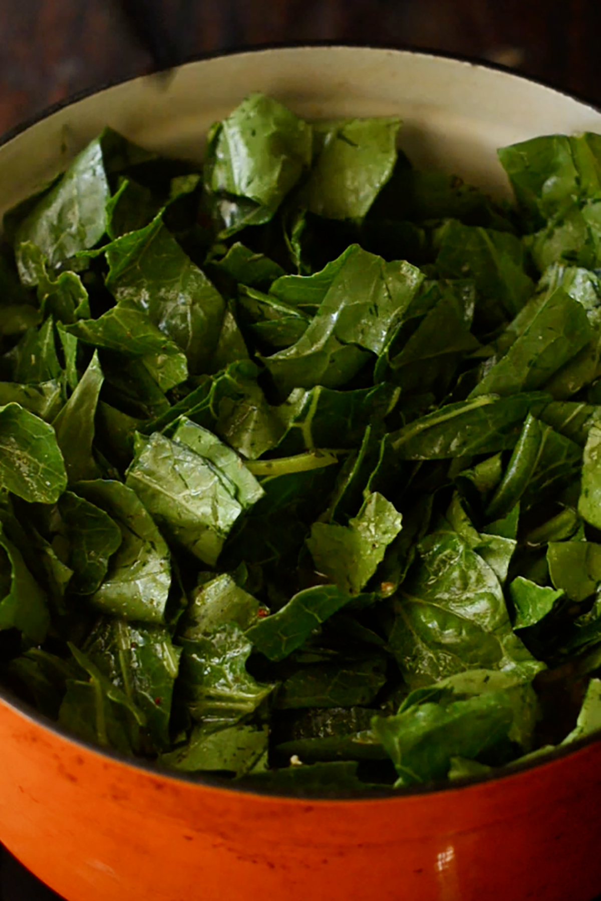 Chopped collard greens in a seasoned liquid in an enameled cast iron dutch oven.