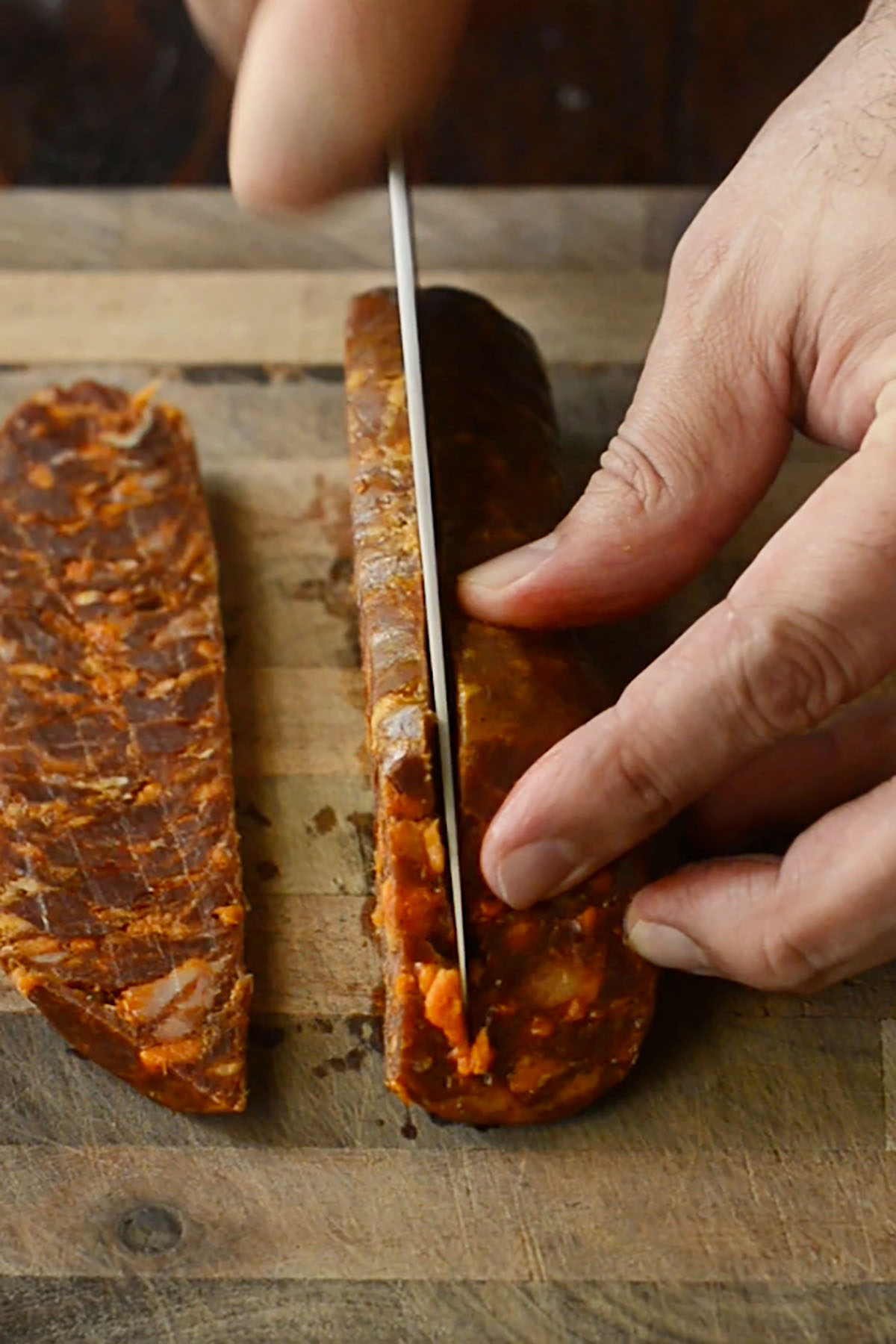 Chorizo salami being sliced on a wood cutting board.