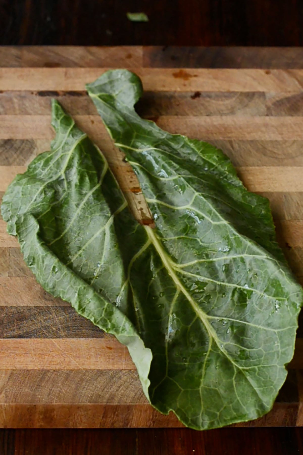 A destemmed collard green leaf on a wood cutting board.
