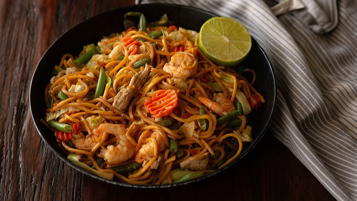 Pancit canton served with a side of fresh lemon wedges in a deep dish plate.