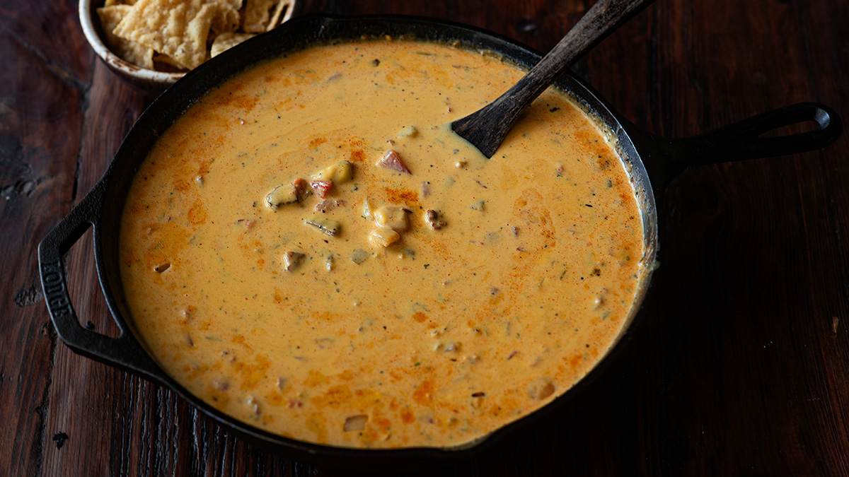Smoked queso served in a cast iron skillet with a wooden spoon and tortilla chips on the side.