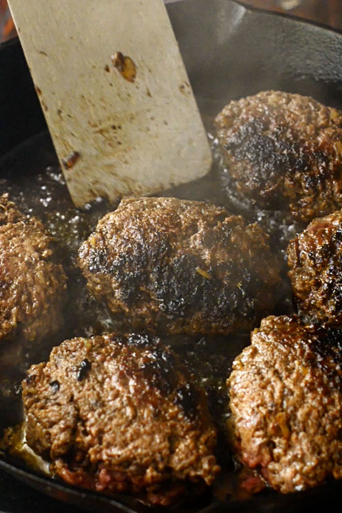 Hamburger steaks cooking in a cast iron skillet.