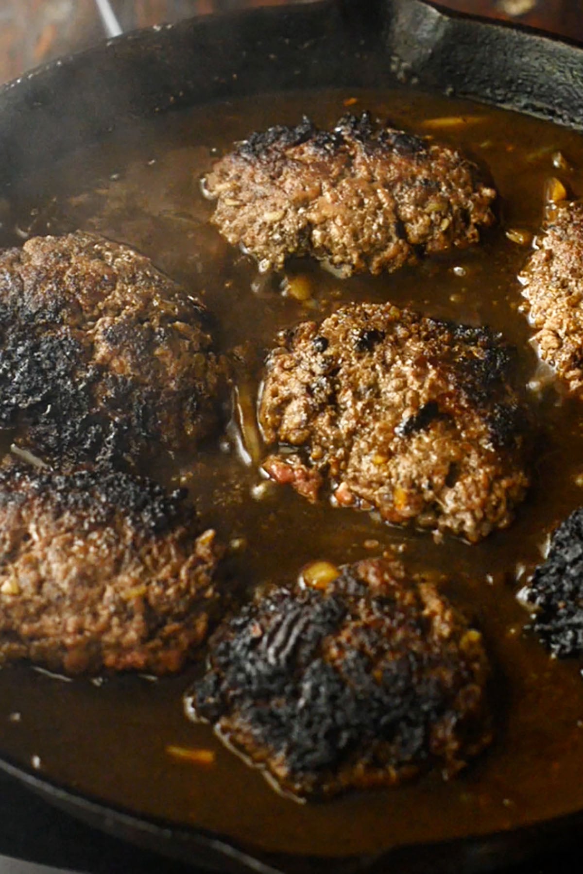 Hamburger steaks and brown onion gravy simmering in a cast iron skillet.