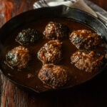 Hamburger steaks with a dark brown beef onion gravy in a cast iron skillet.