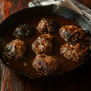 Hamburger steaks with a dark brown beef onion gravy in a cast iron skillet.