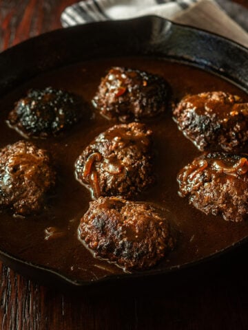 Hamburger steaks with a dark brown beef onion gravy in a cast iron skillet.