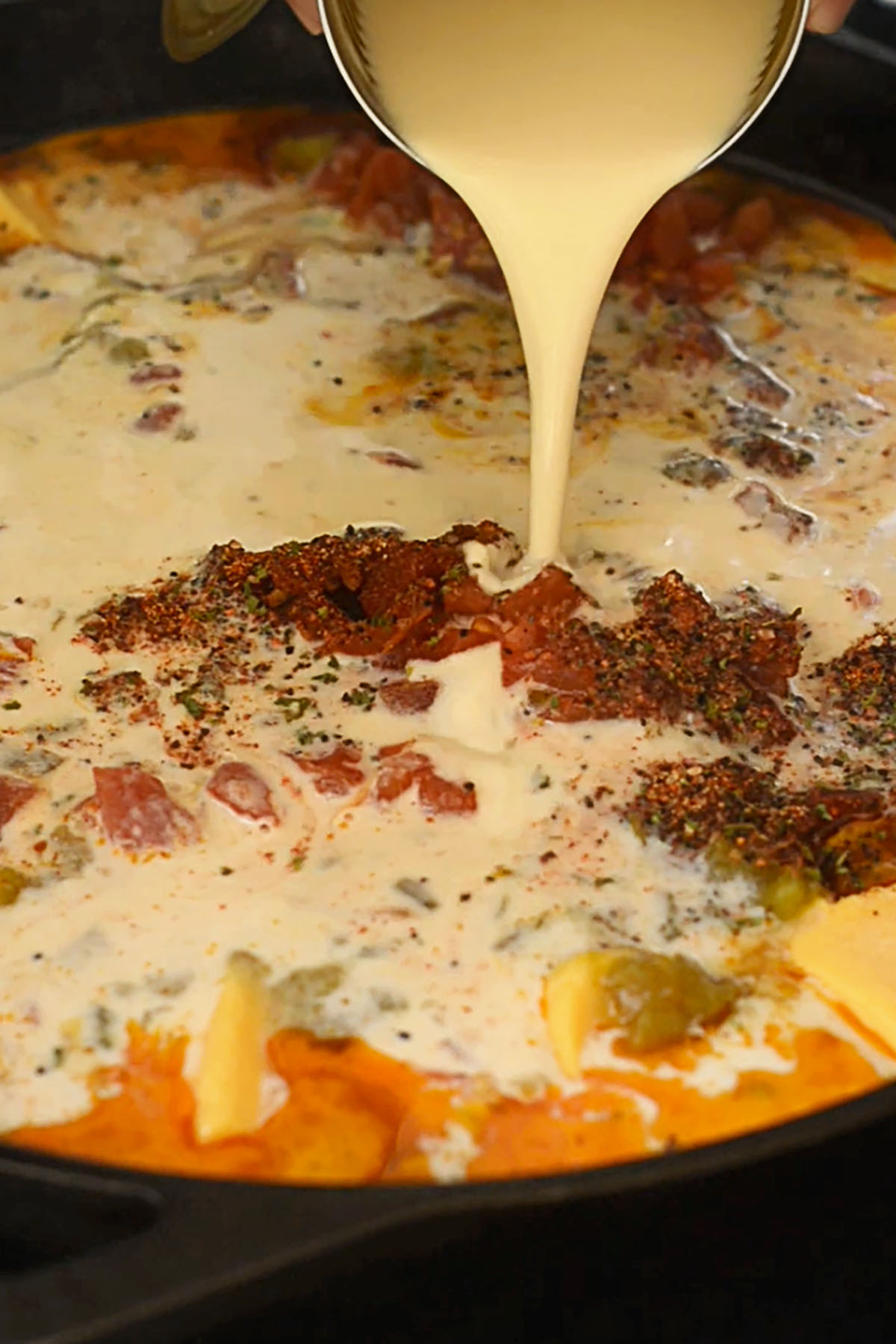 Milk being poured into queso ingredients in a cast iron skillet on a Big Green Egg smoker.