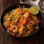 Pancit canton served in a black deep dish plate and garnished with a fresh sliced lime wedge.