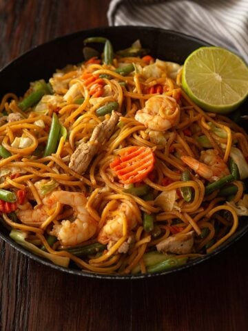 Pancit canton served in a black deep dish plate and garnished with a fresh sliced lime wedge.