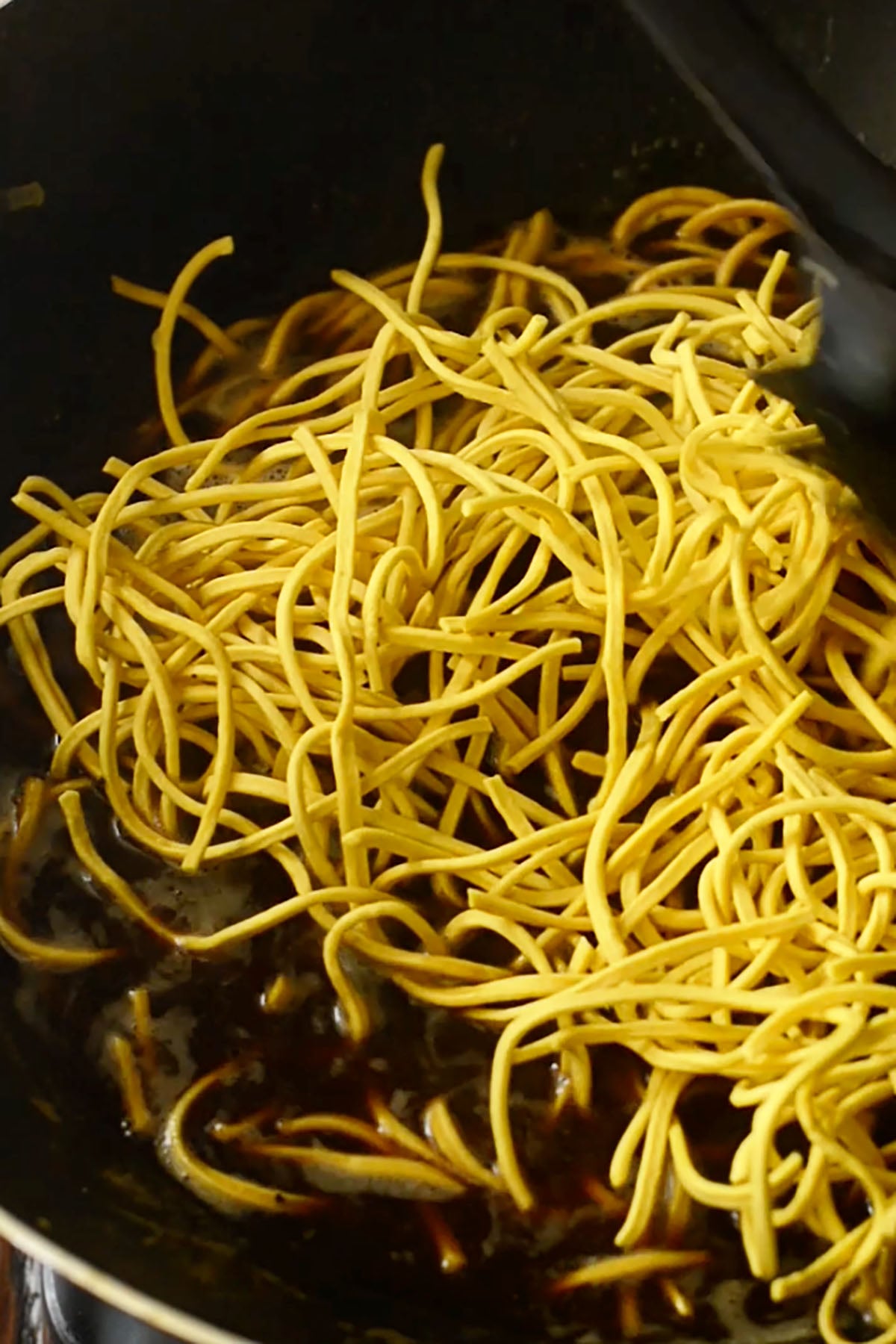 Pancit canton wheat-flour noodles being stirred into a steaming sauce in a wok.