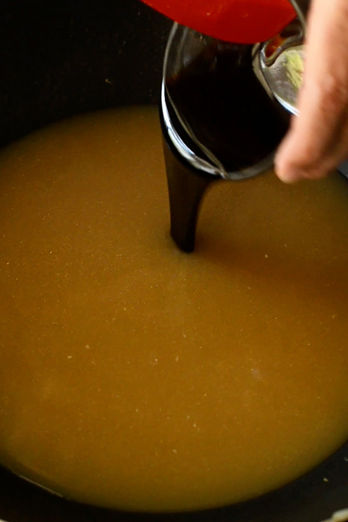 Oyster sauce being poured into a chicken stock in a wok.
