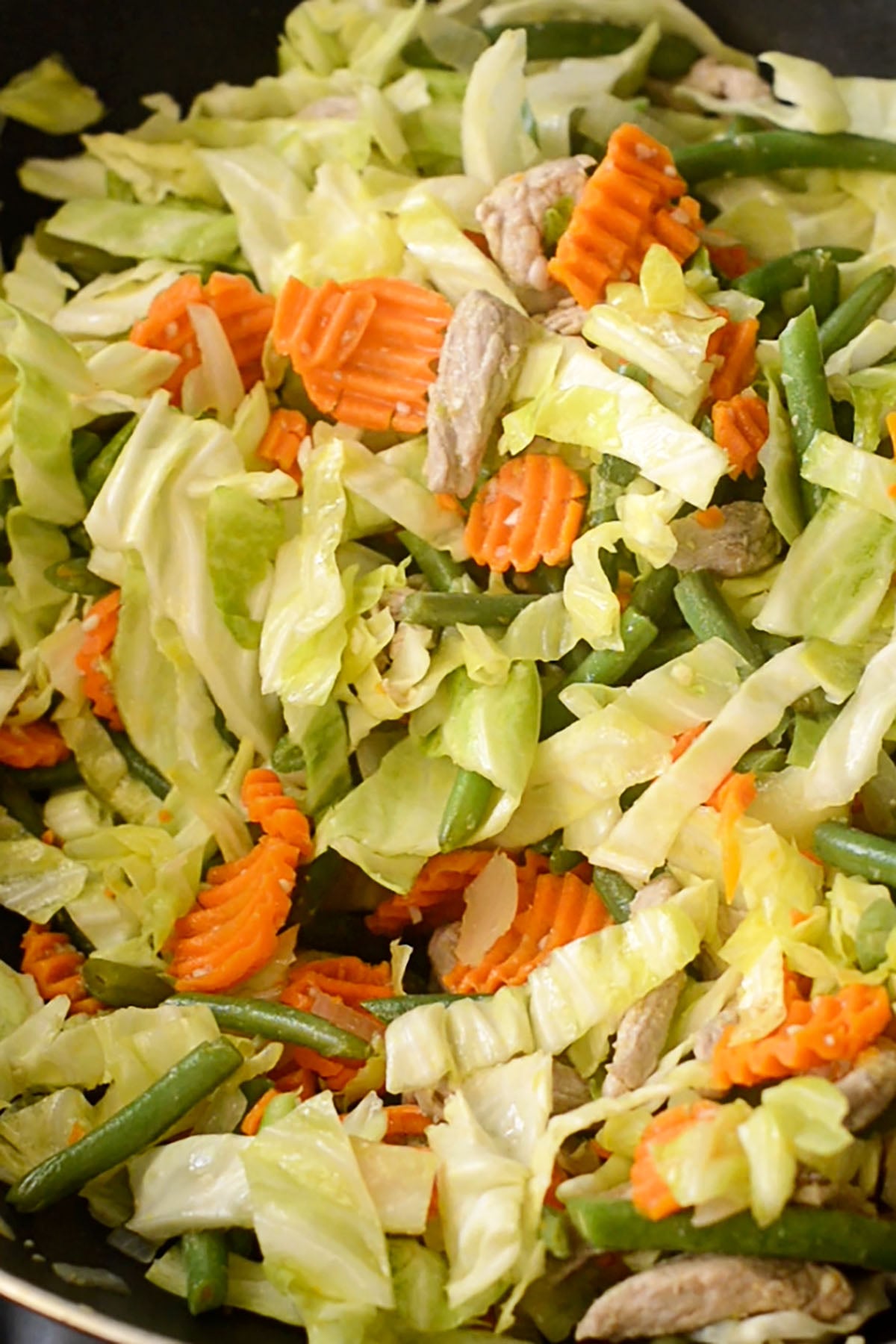 Cabbage, carrots, and green beans combined with pork and onions cooking in a wok.