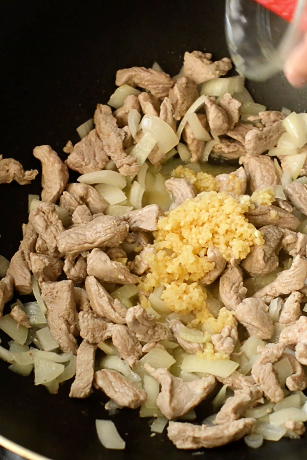 Slice pork tenderloin with diced onion and fresh minced garlic cooking in a wok.