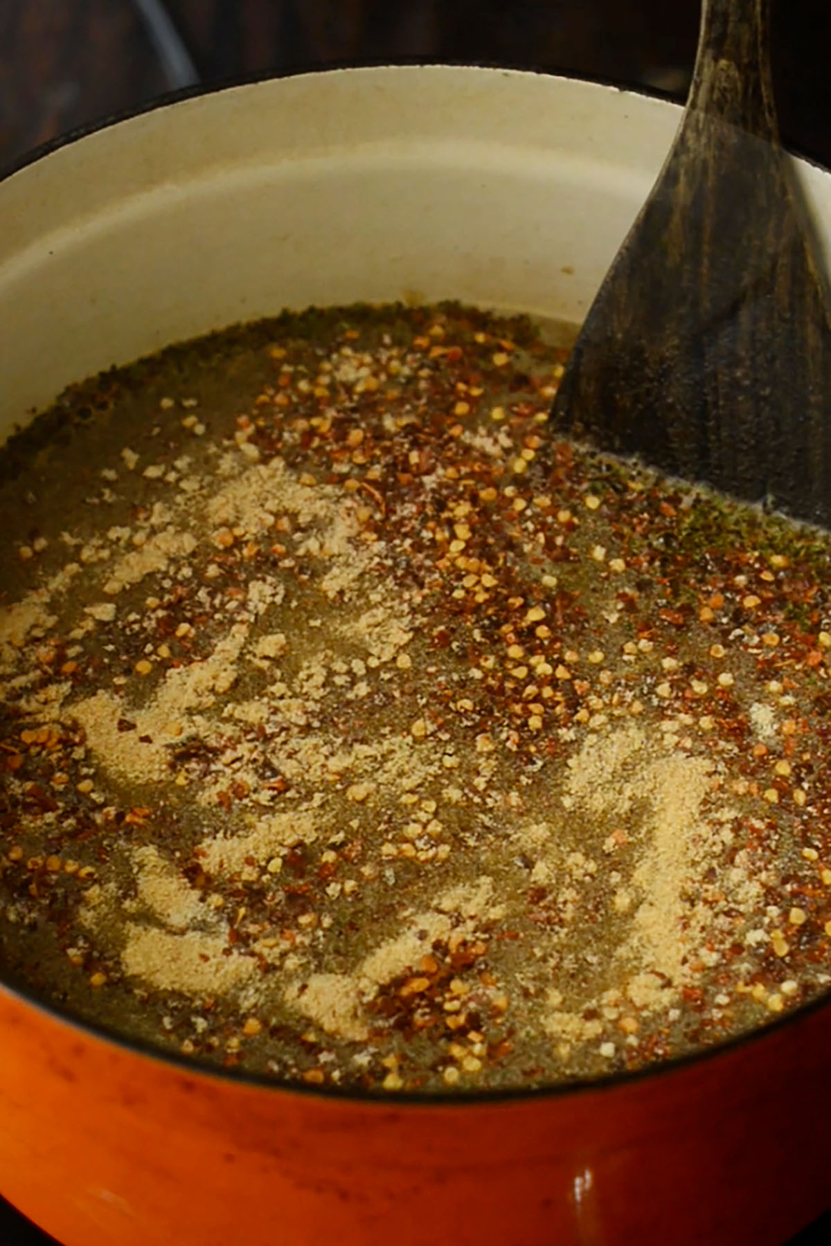 Chicken stock and seasonings being stirred together in a cast iron dutch oven.