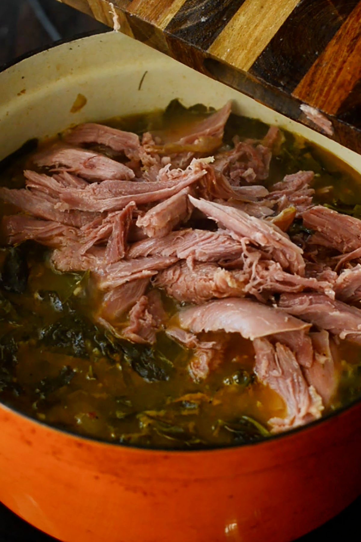 Shredded chunks of smoked turkey leg meat added to a simmering pot of collard greens.