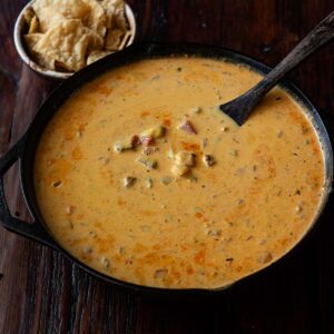 Smoked queso in a cast iron skillet with a wooden spatula and a bowl of tortilla chips.