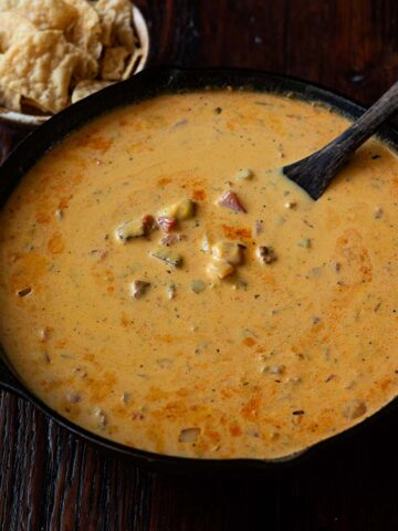 Smoked queso in a cast iron skillet with a wooden spatula and a bowl of tortilla chips.
