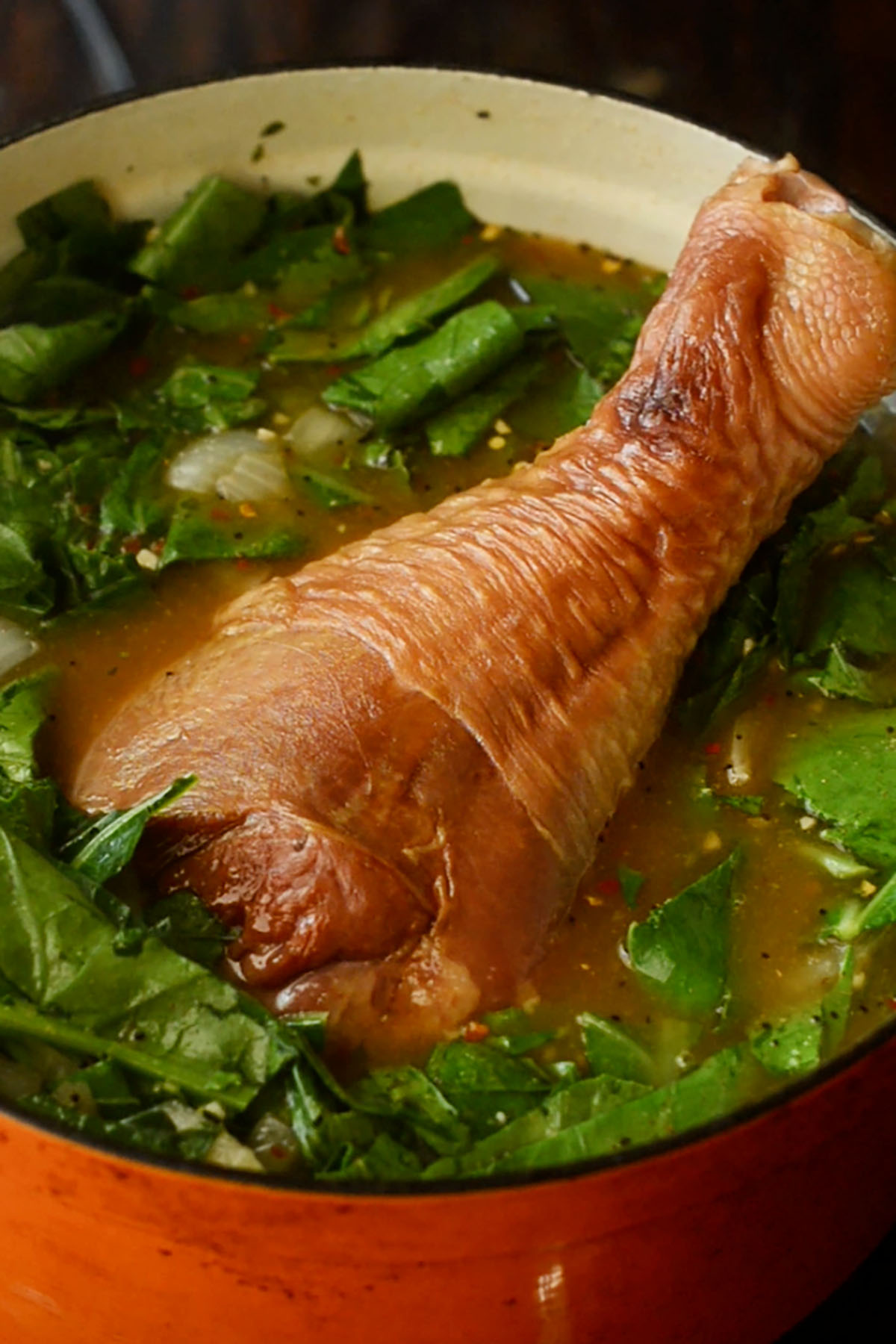 A whole turkey leg nestled into a pot of simmering collard greens and pot likker.