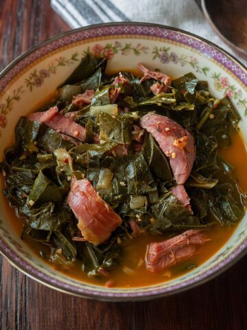 Collard greens with chunks of smoked turkey legs served in a vintage decorative bowl.